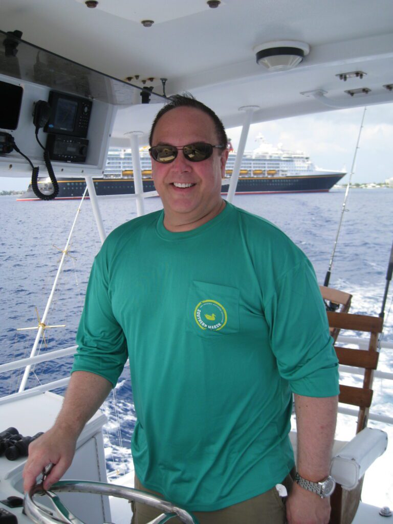 Image of James McCabe at helm of 65ft hatteris fishing boat, wearing sunglasses and long sleeve green pullover